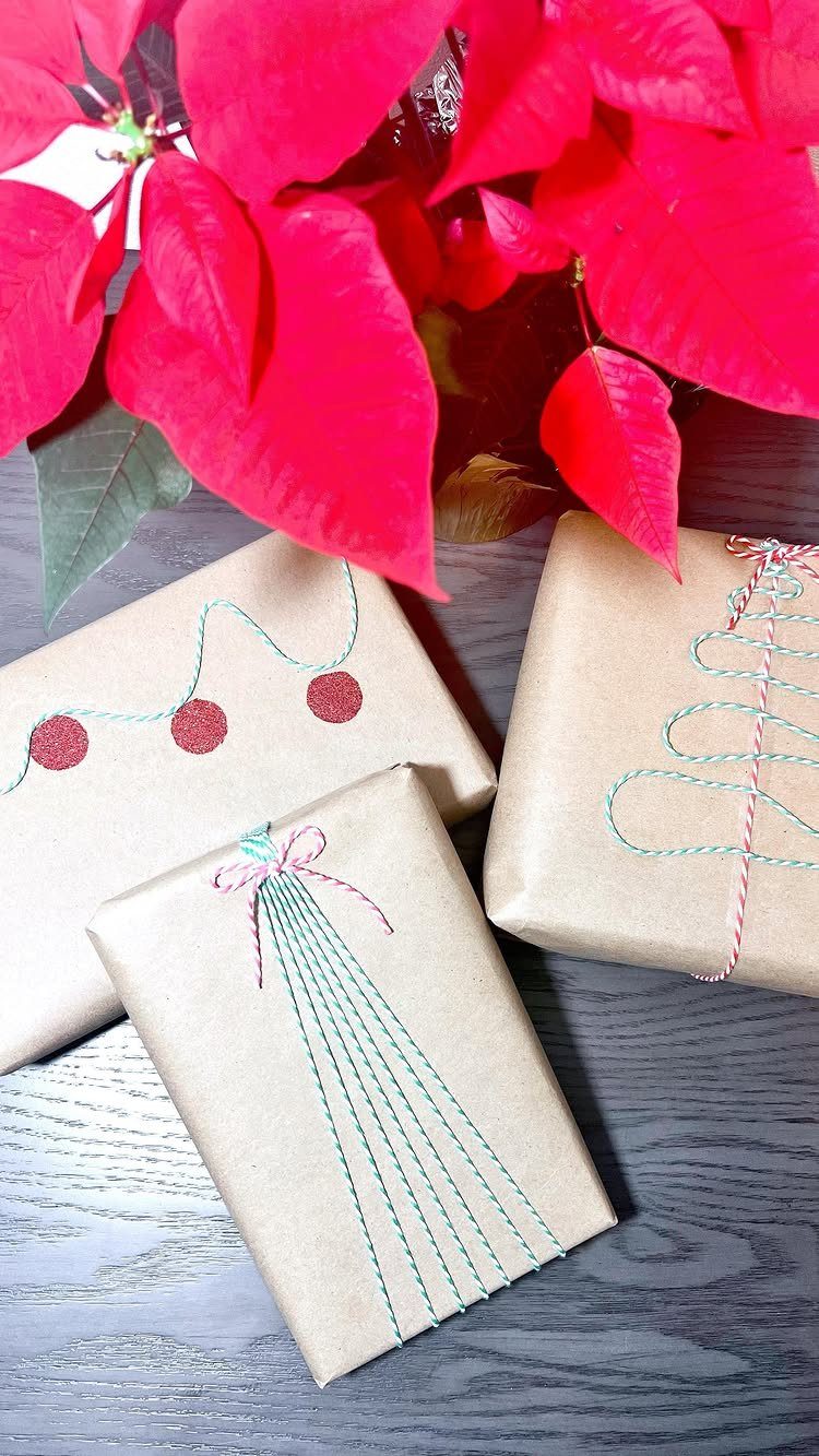 Brown kraft paper wrapped gifts with teal decorative stitching and red poinsettia leaves.