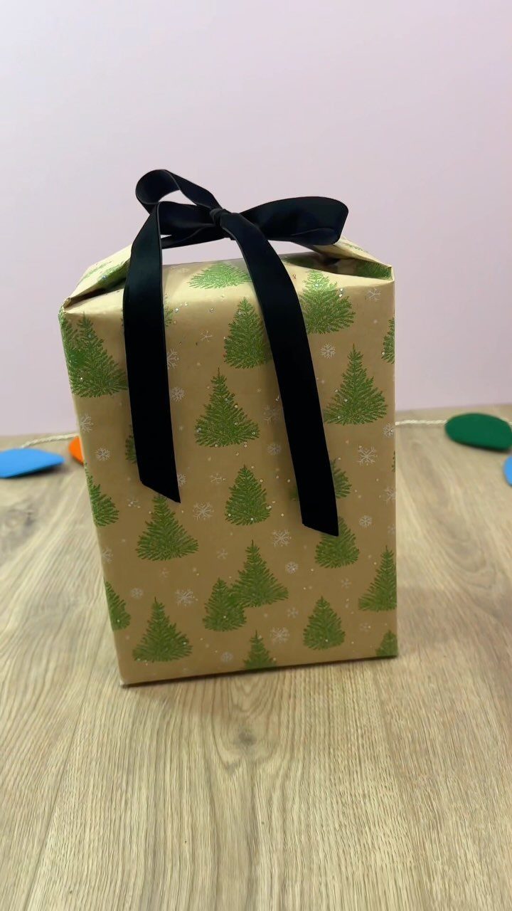 Handmade gift bag from tree-patterned wrapping paper tied with a black satin bow.