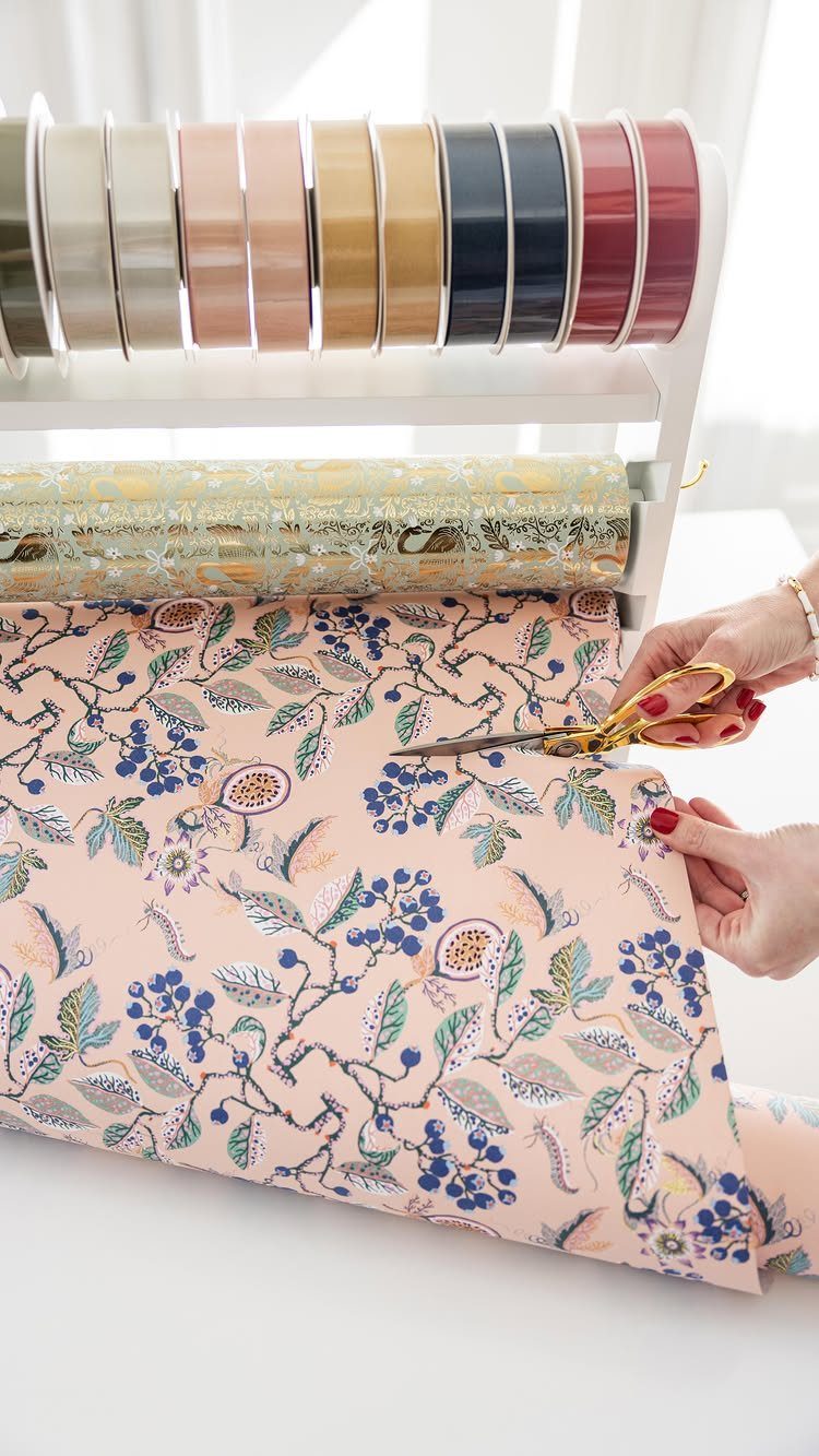Hands cutting pink floral wrapping paper from a white ribbon and paper organizer.