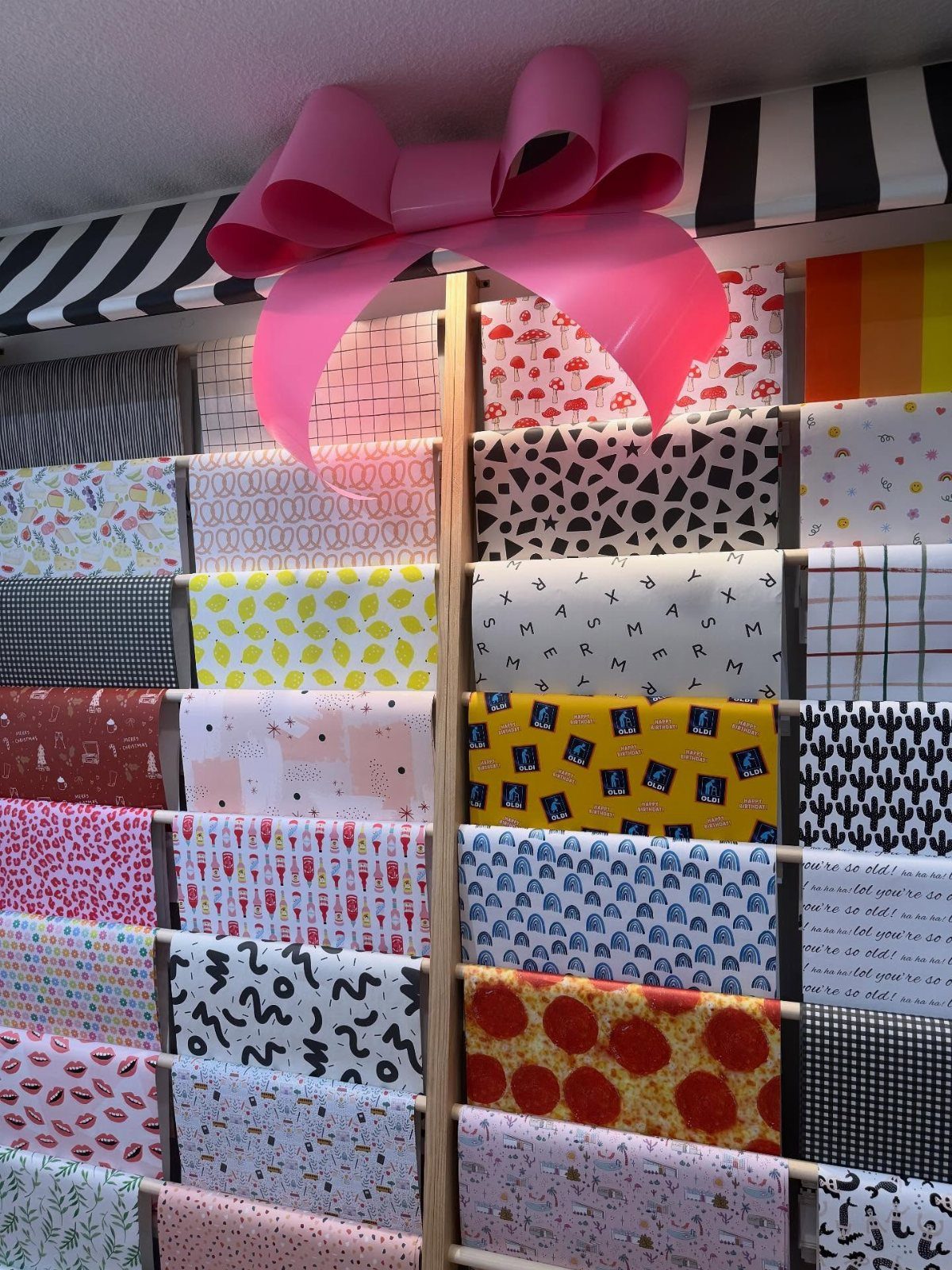 Wooden rack holding various rolls of patterned wrapping paper with a large pink bow.