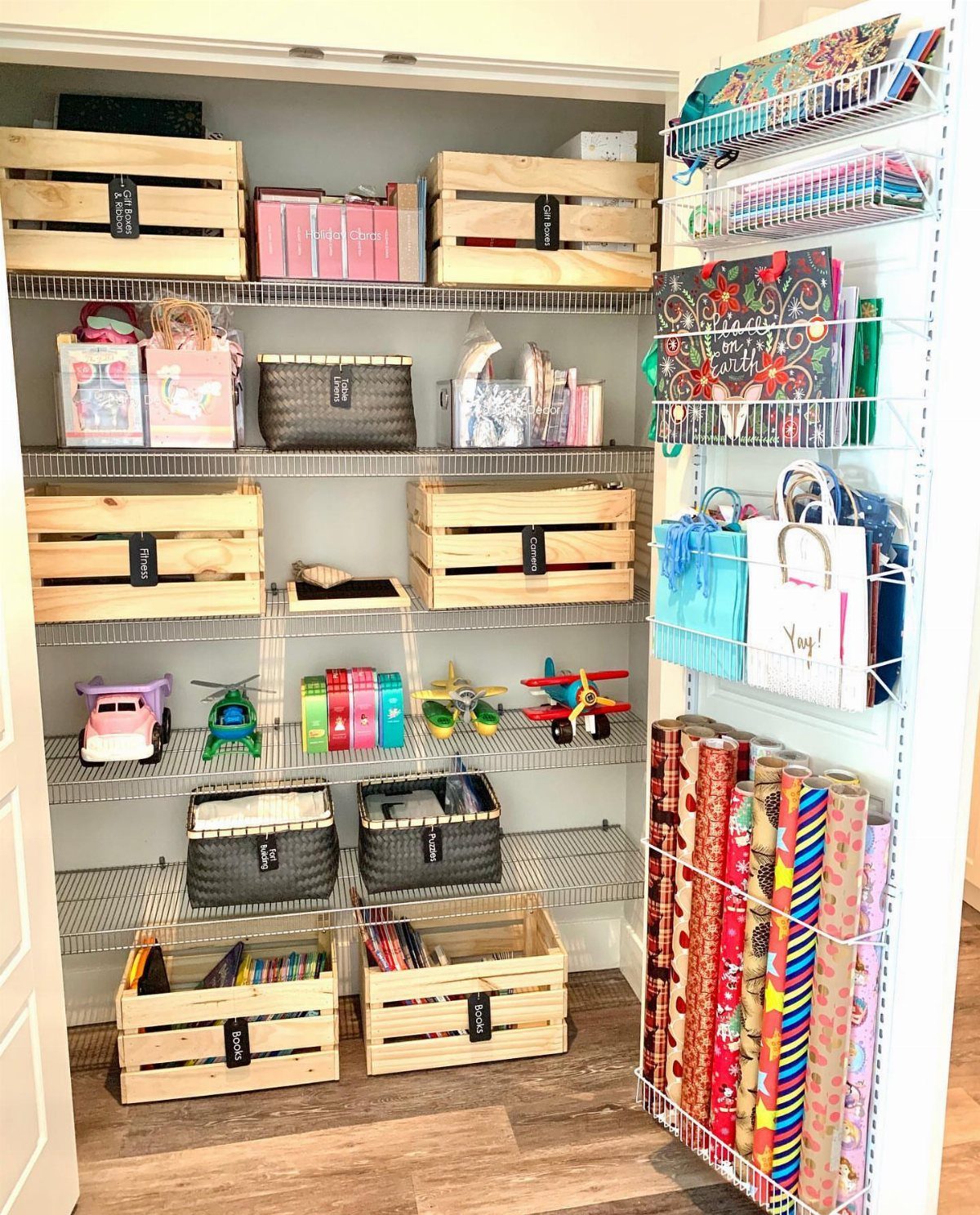Over-the-door wire organizer holding colorful wrapping paper rolls and gift bags in a closet.