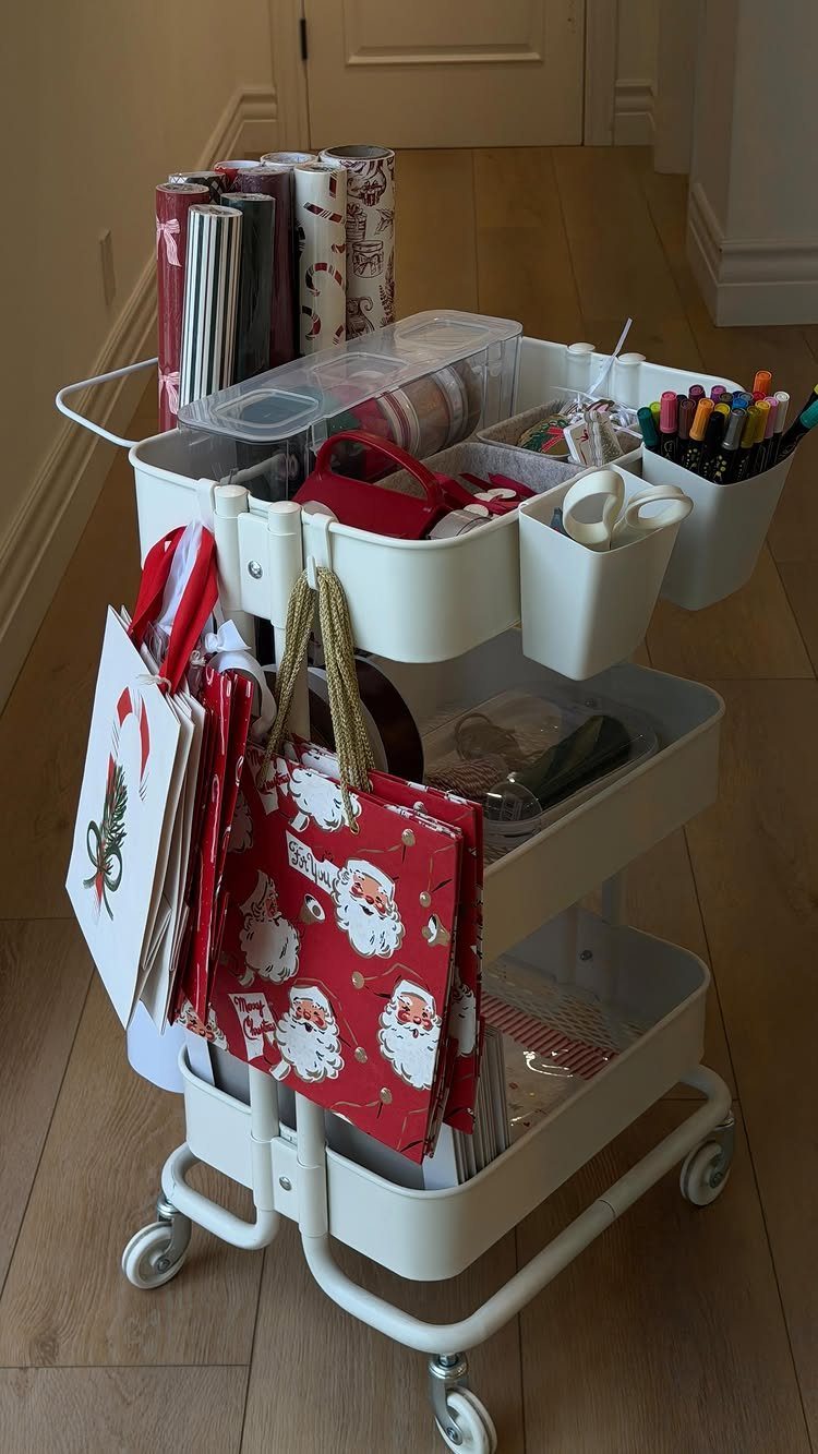 White rolling cart organized with wrapping paper, ribbons, markers, and Christmas gift bags.