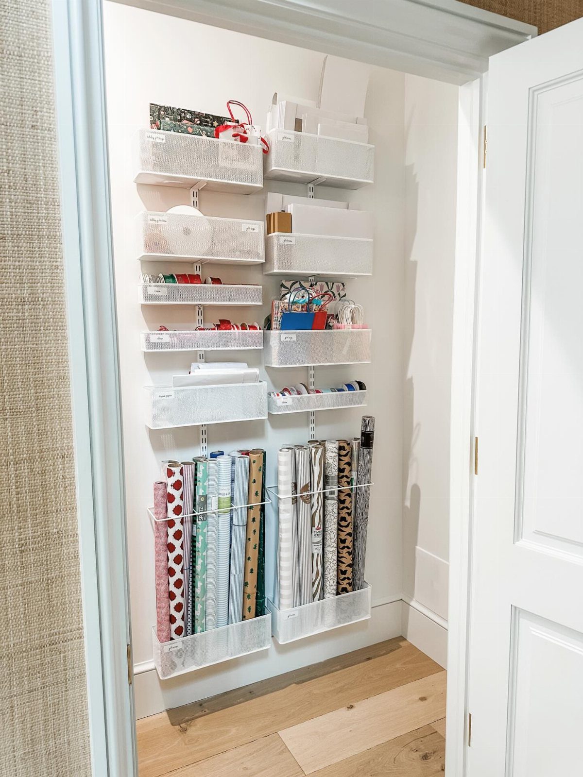 Wall-mounted white baskets organizing rolls of wrapping paper and gift supplies in a closet.