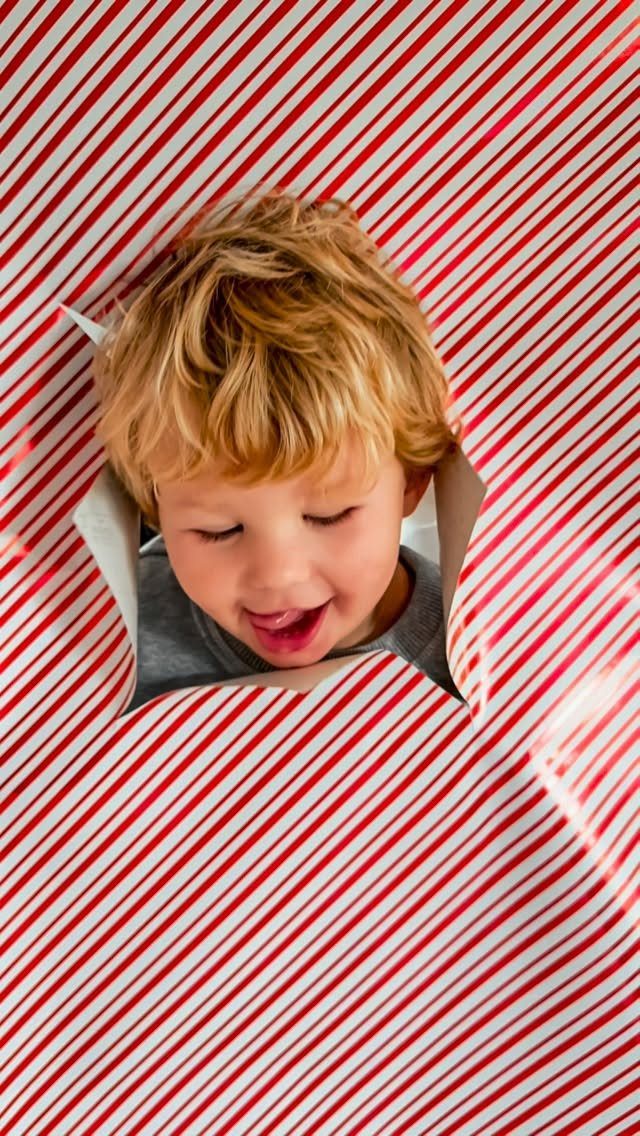Blonde child peeking through a hole in red and white striped wrapping paper