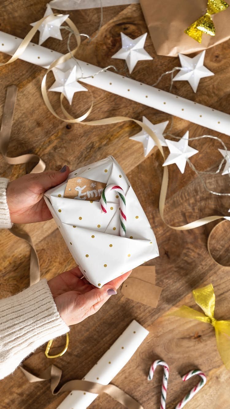 Hands holding a white polka dot wrapped gift with a candy cane topper.