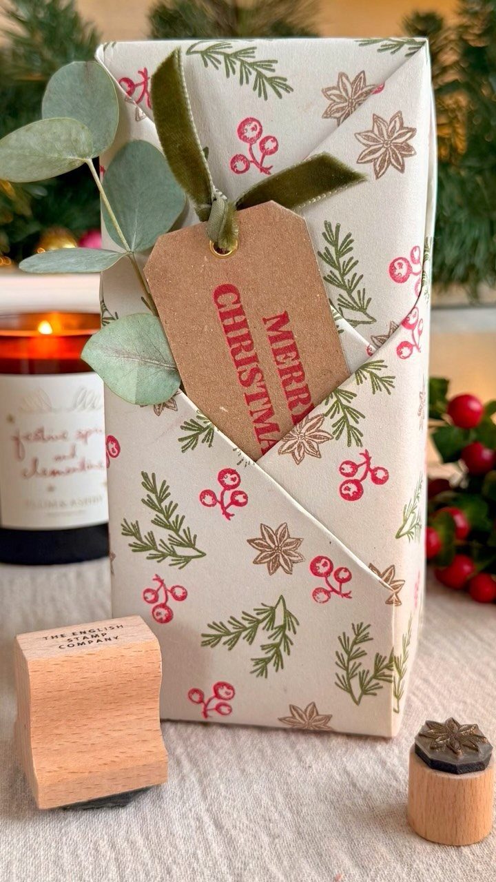 Wrapped gift with red berry patterns, a Merry Christmas tag, and wooden stamps.