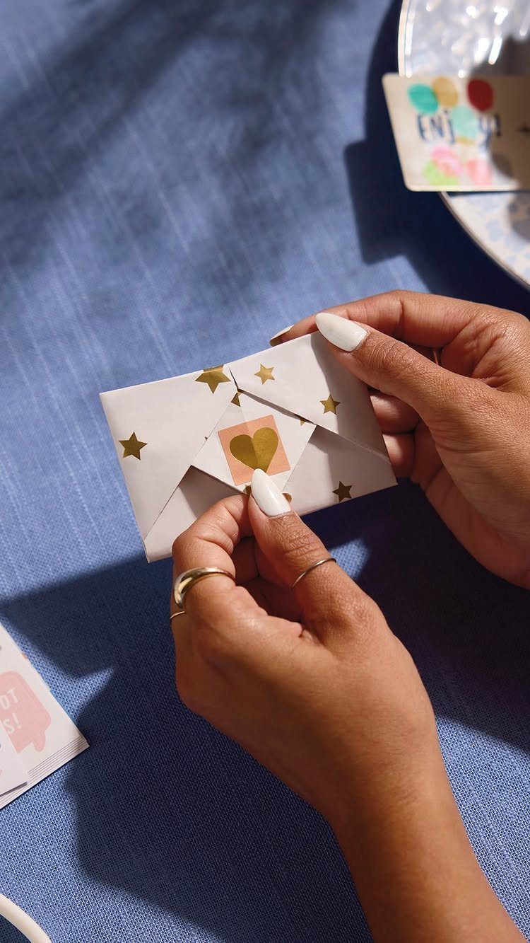 Hands holding a small white star-patterned envelope containing a gold heart card.