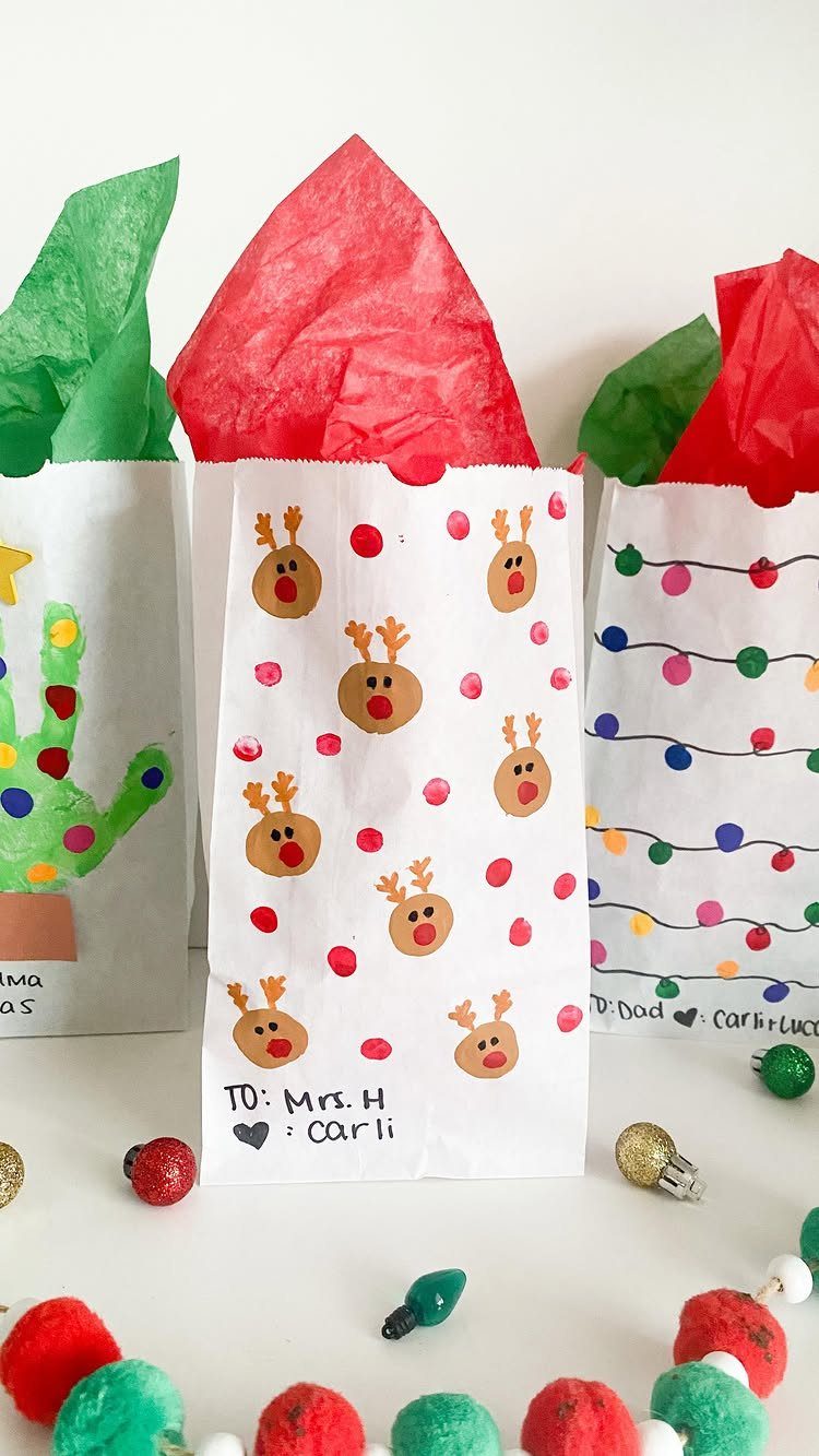 White gift bags featuring thumbprint reindeer faces and colorful tissue paper toppers.