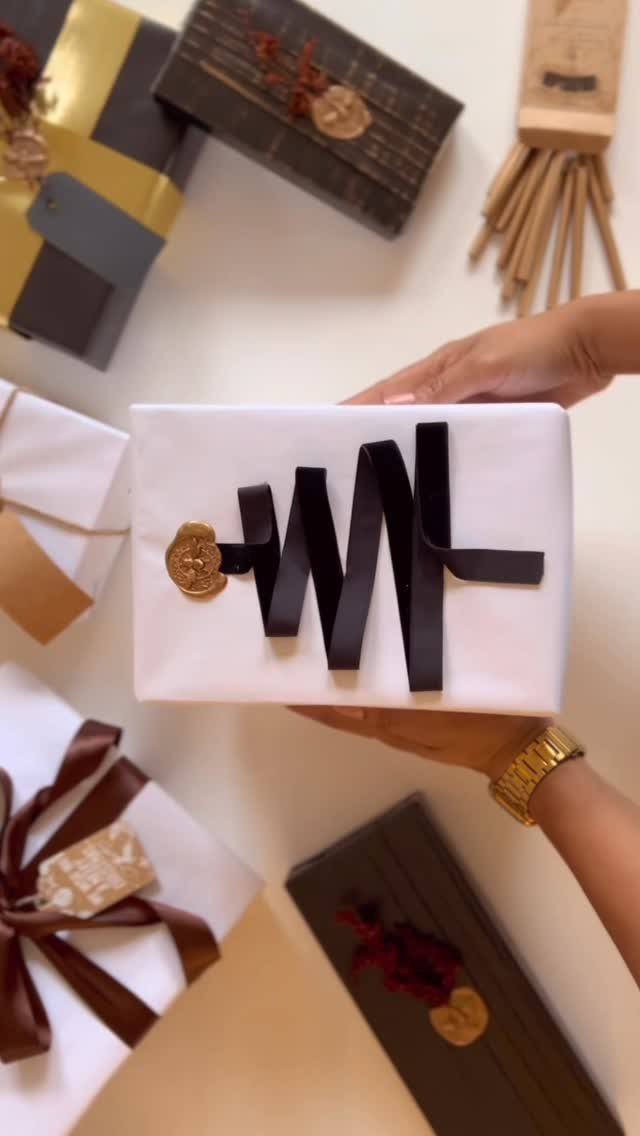 White wrapped gift box with black ribbon and gold wax seal held by hands.