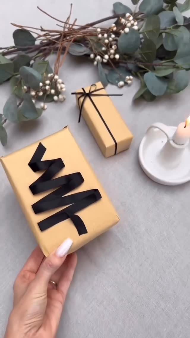 Brown kraft paper wrapped gifts with black ribbons and eucalyptus branches on grey surface